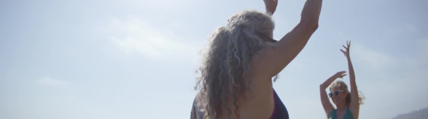 A diverse group of senior women dance with joyful abandon on a sunny beach in slow motion