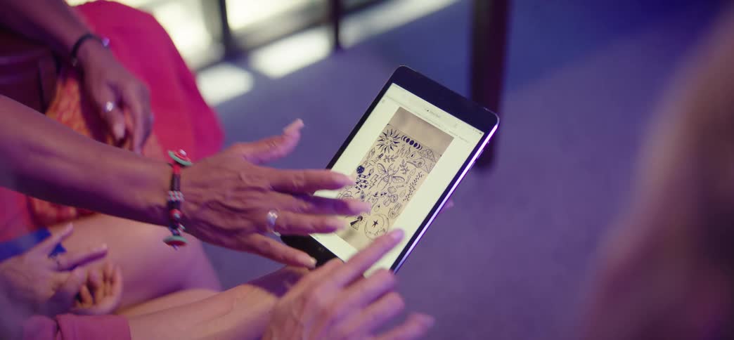 Close-up of hands scrolling through and pointing at a digital catalog of tattoo flash art on a tablet