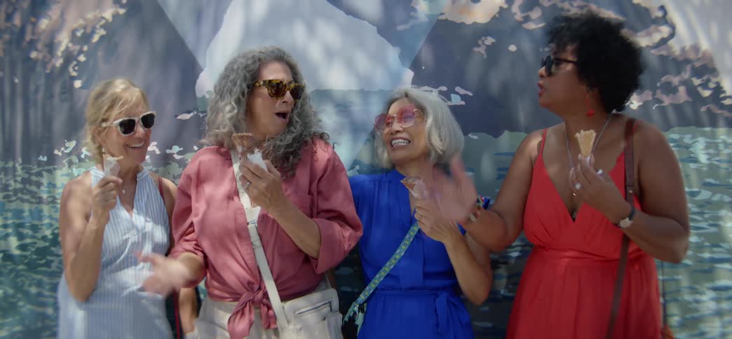 A diverse group of joyful senior female friends laugh and chat while eating ice cream cones together outdoors