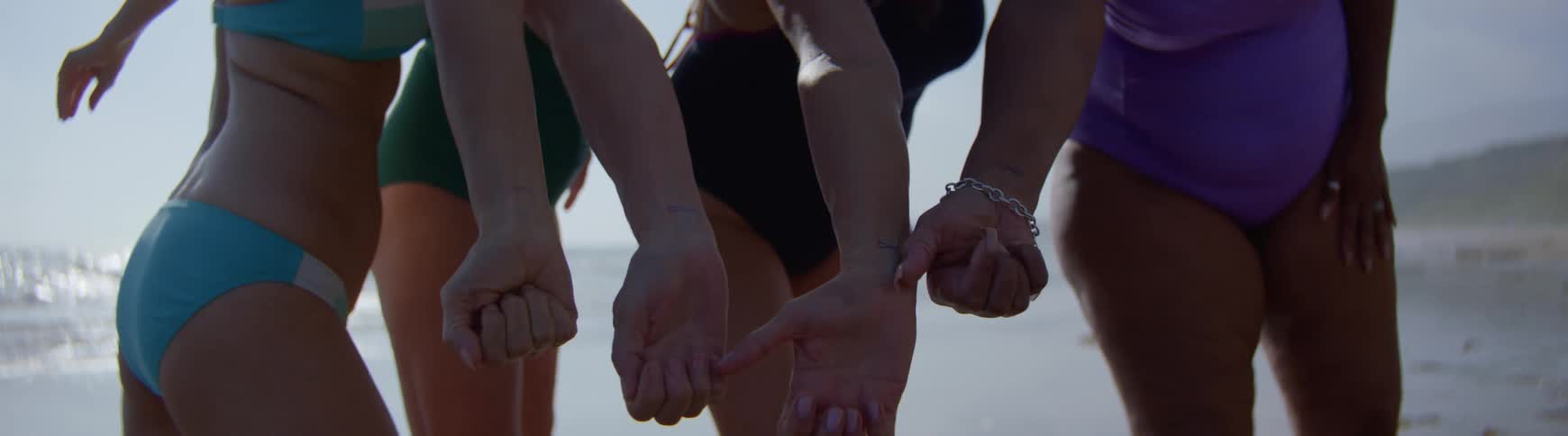 Close-up of female friends in swimsuits showing off their matching wrist tattoos on the beach