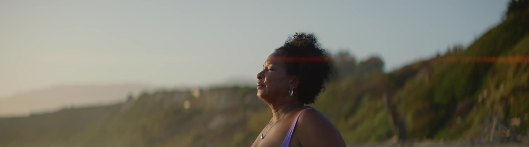 A peaceful woman with her eyes closed takes a deep meditative breath while soaking in the golden hour sunlight
