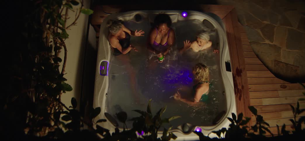 Four diverse female friends laugh and playfully spray champagne while enjoying a celebratory night in a hot tub