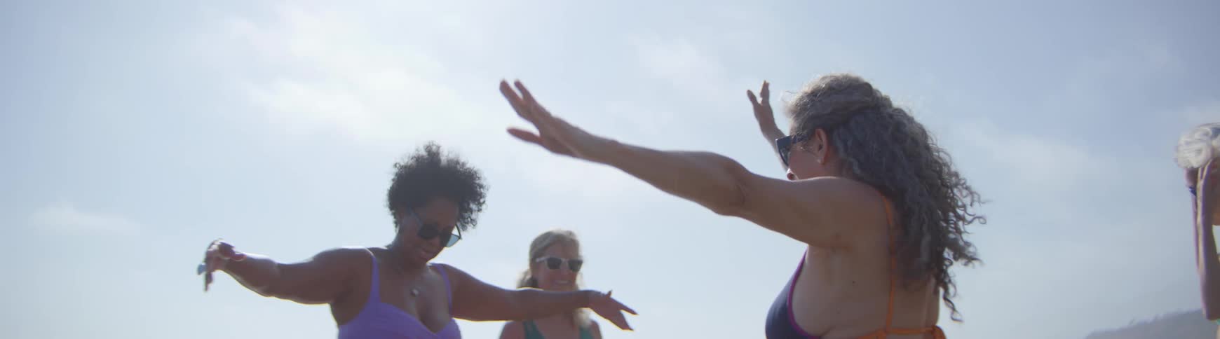 Carefree senior women friends in swimsuits dance and laugh together on a sunny day in slow motion