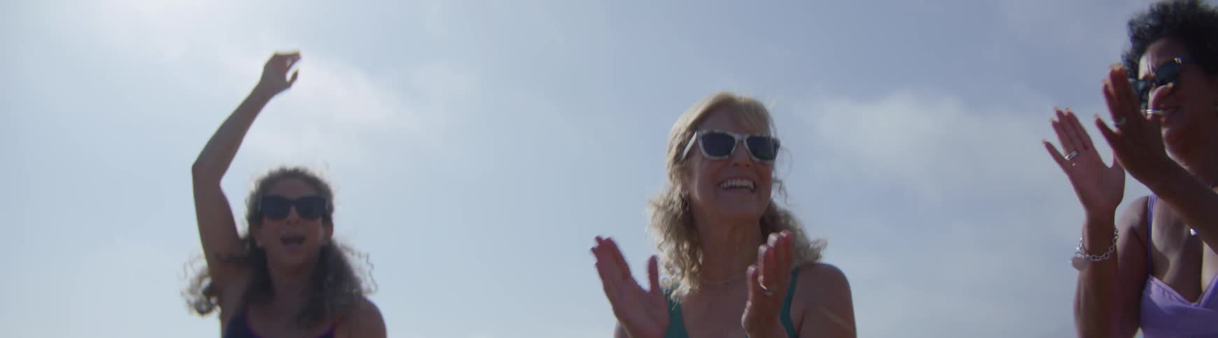 A group of senior women with matching friendship tattoos celebrate on the beach, dancing and high-fiving in slow motion