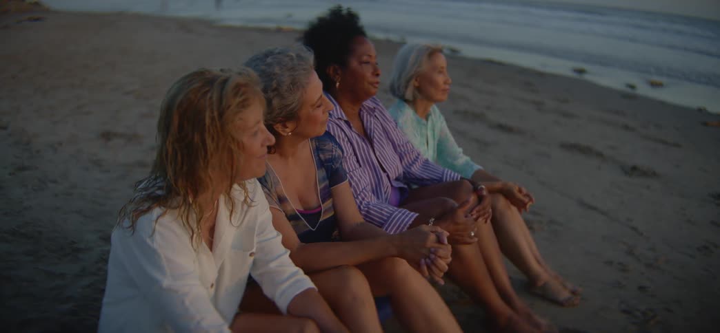 A group of diverse senior women friends share a quiet, contemplative moment on the beach at sunset