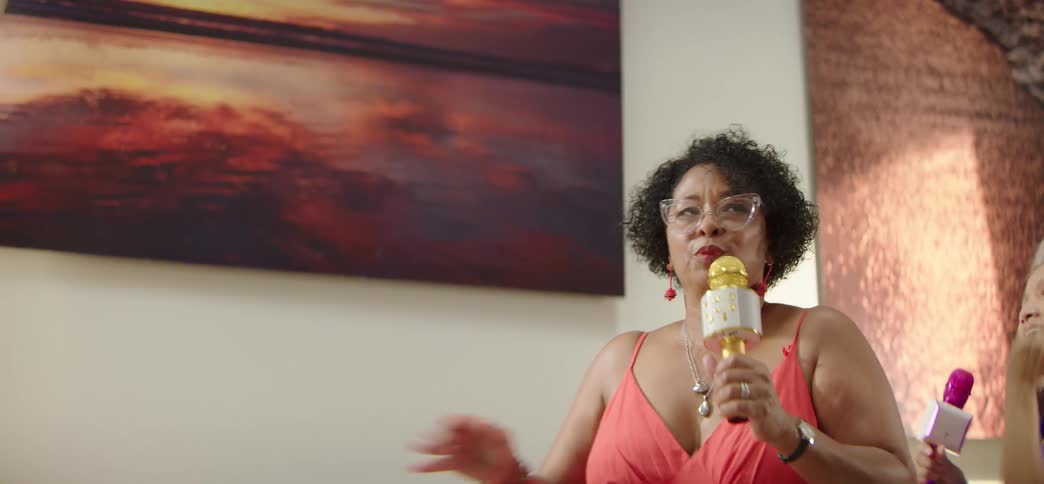Two diverse elderly women have a blast singing and dancing karaoke together in their living room in slow motion