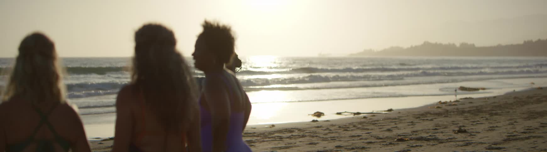 Surfers on the beach watch a lone horseback rider by the ocean's edge during a hazy golden sunset