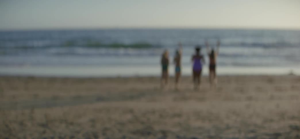 An intentionally blurred shot shows four women of different ages and sizes running towards the ocean in slow motion