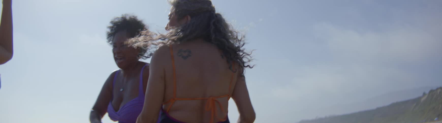 Slow motion shot of diverse mature women with matching infinity tattoos dancing and celebrating friendship on the beach