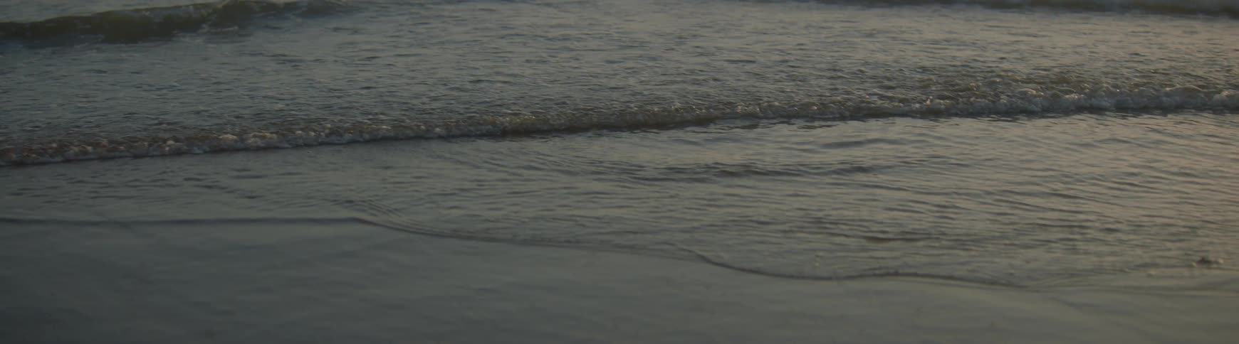 Gentle ocean waves slowly recede from the wet, dark sand on a tranquil beach at dusk