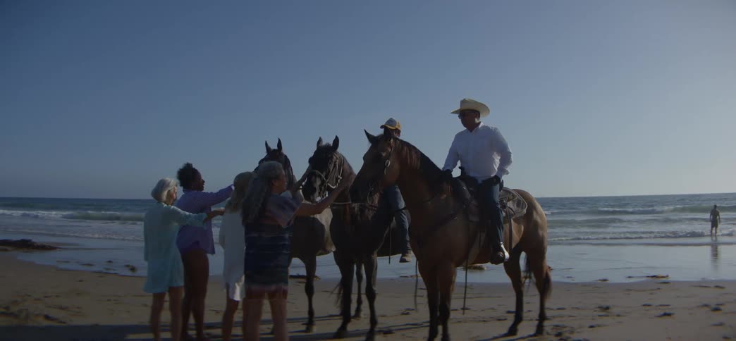 A group of friends greet men on horseback on a sunny beach before their ride along the ocean waves