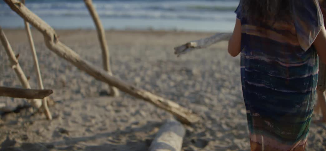 A group of active senior friends work together to build a driftwood shelter on a sandy beach by the ocean