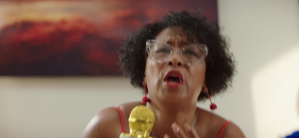 An expressive older woman sings passionately into a gold microphone and dances during a fun karaoke party