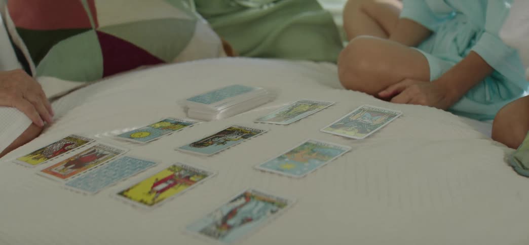 A woman interprets a tarot card spread for her friends while relaxing on a bed in robes