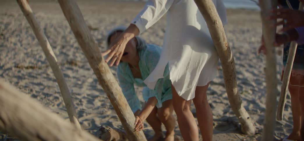 A group of diverse senior women friends collaborate to build a driftwood shelter on the beach