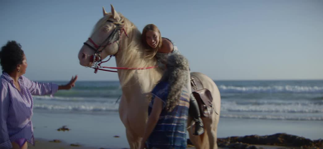 A diverse group of smiling women enjoy a leisurely day on the beach, petting their beautiful horses by the ocean