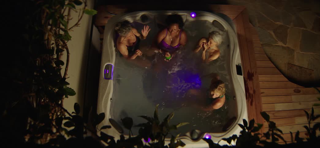 Fun-loving mature female friends have a champagne party in an outdoor jacuzzi at night