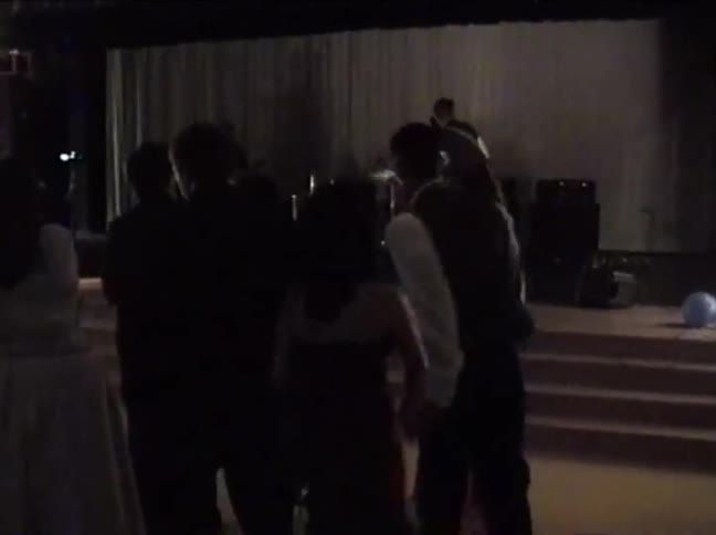 Vintage VHS footage shows teenagers in formal attire at a school dance watching a live band on stage
