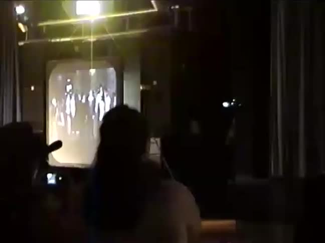 Vintage VHS footage captures a singer performing on a dark stage in front of an audience and next to an old television screen