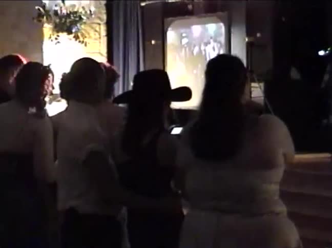 Vintage VHS footage captures guests at a wedding reception watching a slideshow presentation on a screen