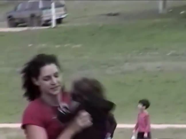 A loving mother smiles as she playfully lifts her young toddler in the air and gives them a kiss in a park