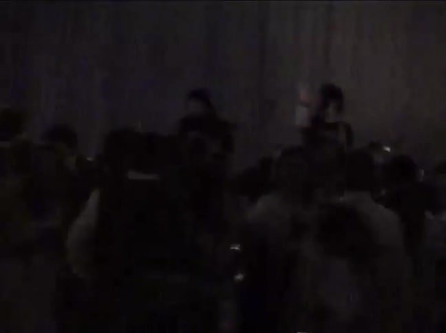 Grainy, low-light vintage footage shows a crowd moshing to a live rock band at an underground concert
