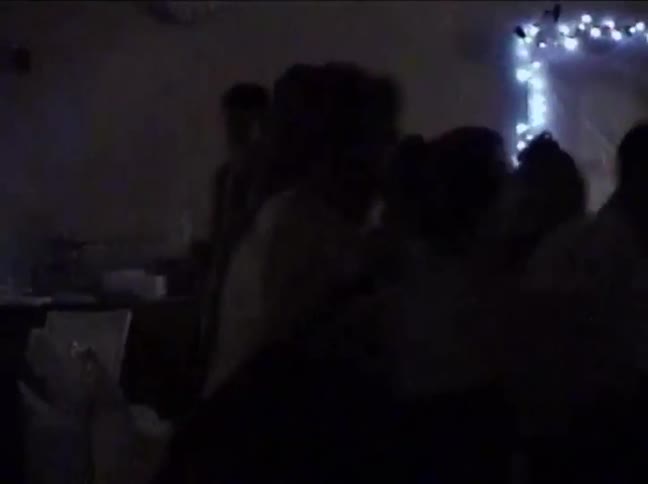 Vintage VHS footage captures silhouettes of people dancing at a lively party in a dimly lit room