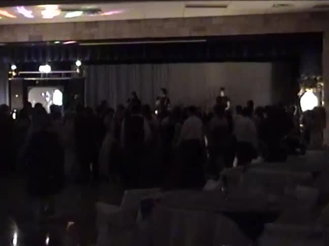 Vintage VHS footage shows a crowded dance floor at a party or wedding reception with a live band playing on stage
