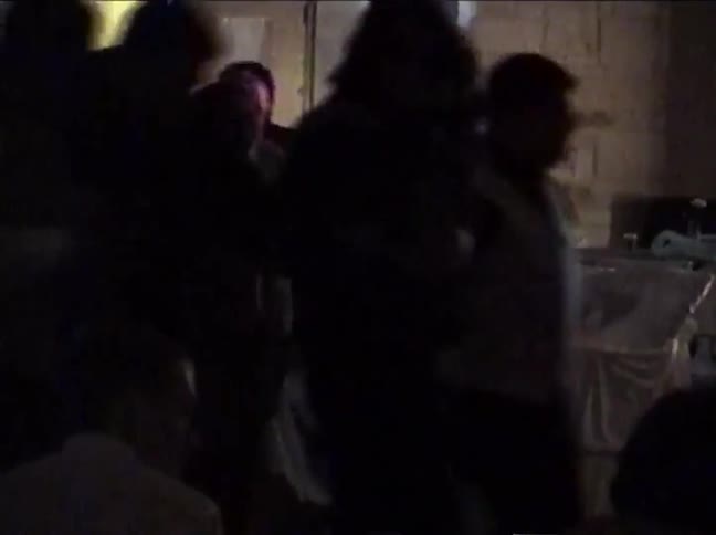 Grainy vintage footage shows people dancing and socializing at a party in a dimly lit venue