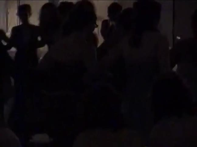 Silhouettes of couples slow dance at a dimly lit formal party in grainy vintage footage