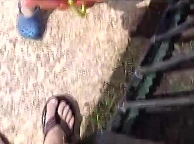 A cute toddler with wet hair looks up and smiles sweetly while holding a red bucket in a sandbox