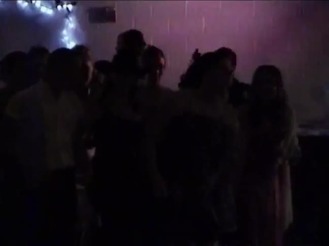 Grainy, vintage 1990s VHS footage shows a group of silhouetted young people dancing at a party in a dimly lit room
