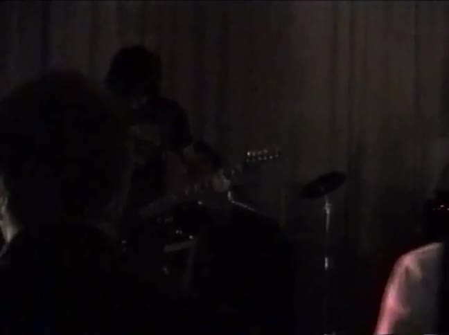 Vintage VHS footage captures a rock band's energetic performance on a dark stage from an audience perspective