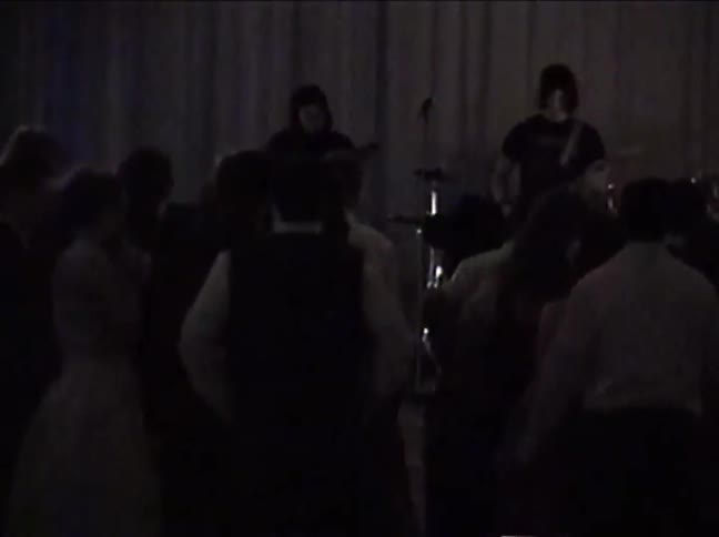 Vintage VHS footage shows a rock band performing as teenagers slow dance at a school prom
