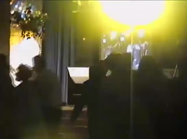 Vintage VHS footage captures the silhouettes of guests dancing at a dimly lit party or wedding reception
