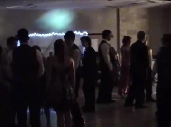 Vintage VHS footage shows silhouetted teenagers and young adults socializing and dancing at a school prom with colorful spotlights