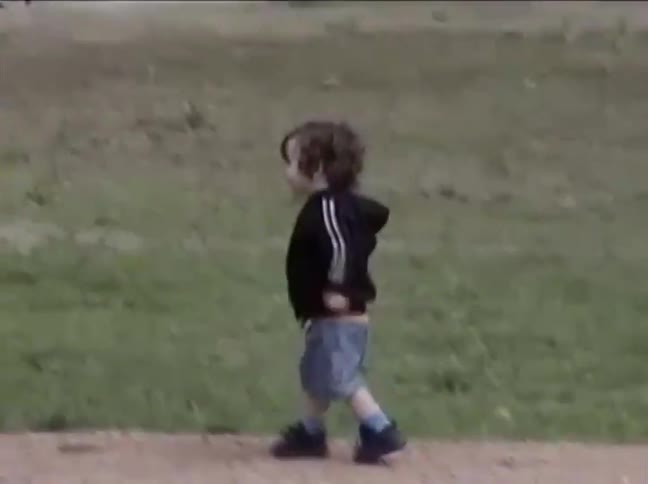 Toddler with curly hair walks and runs across a grassy park in casual outdoor play