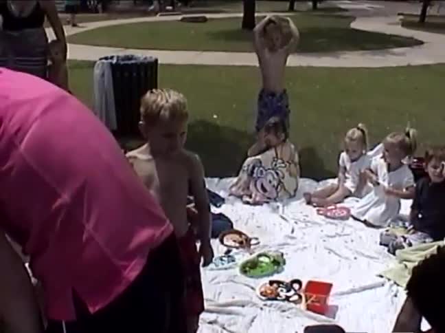 Vintage home movie footage of children and adults enjoying a sunny picnic in a grassy park