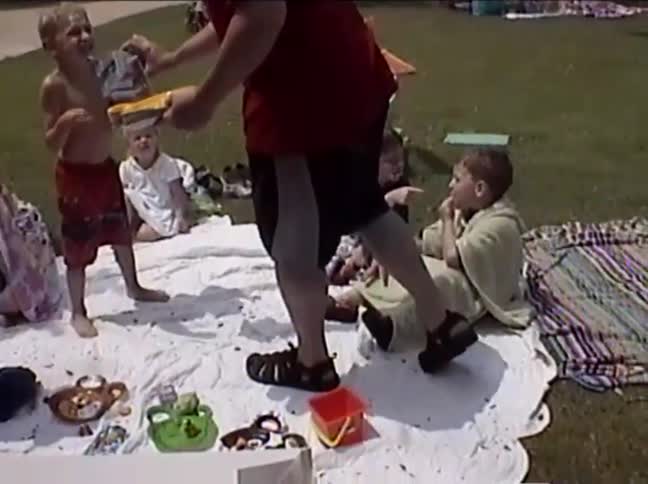 A group of young children in swimsuits excitedly gather for birthday cake during a fun party in the park