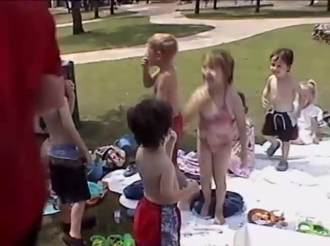 A group of young children in swimwear excitedly play with bubbles at a summer gathering in a park
