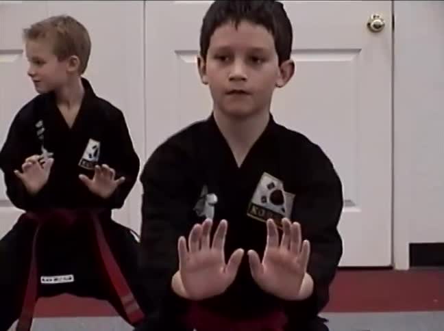 A focused young boy with a red belt holds a difficult martial arts stance during a class in a dojo