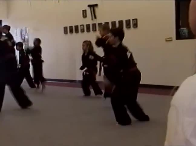Young students in black uniforms practice a synchronized Kuk Sool Won routine during a martial arts class