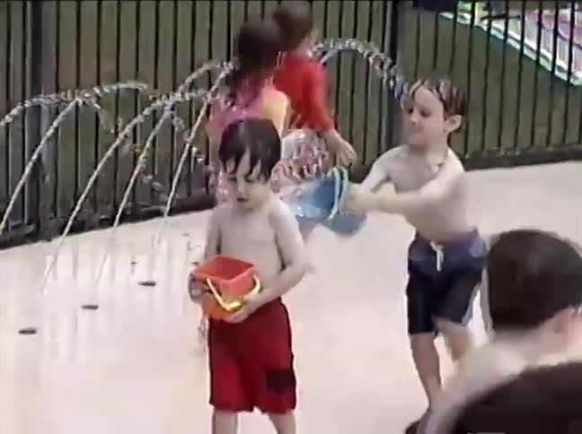 A group of happy children and their parents play in the sprinklers at a splash pad during the summer