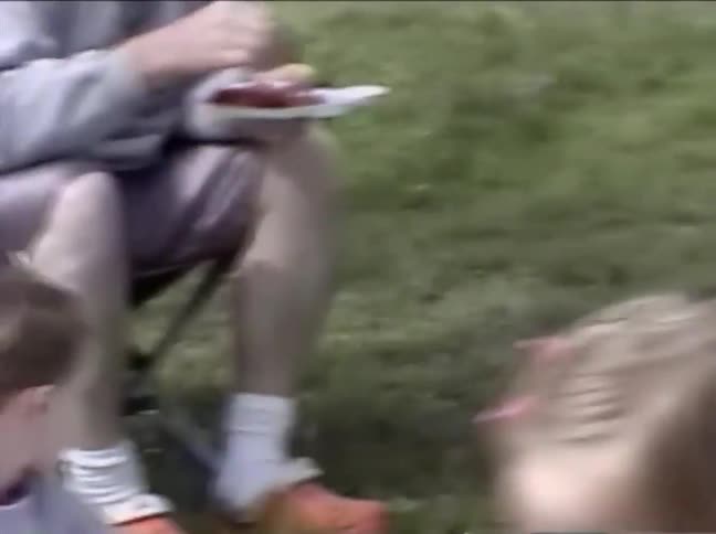 Vintage home video footage of a family and friends enjoying a picnic in a grassy park on a sunny day