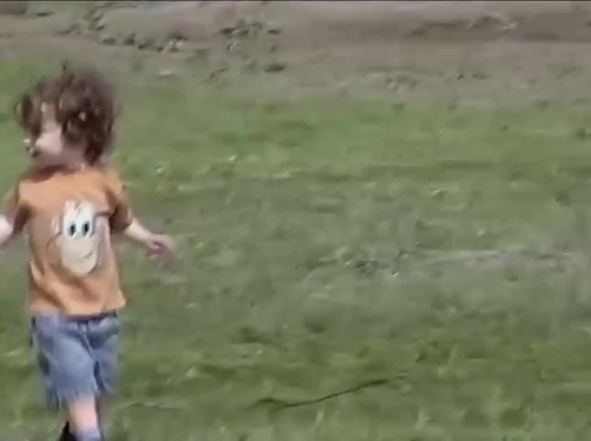 A mother helps her young son take off his jacket before they walk together through a sunny park