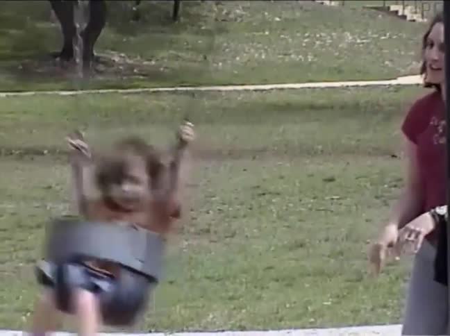 A vintage home movie captures a mother gently pushing her happy toddler on a park swing on a sunny day