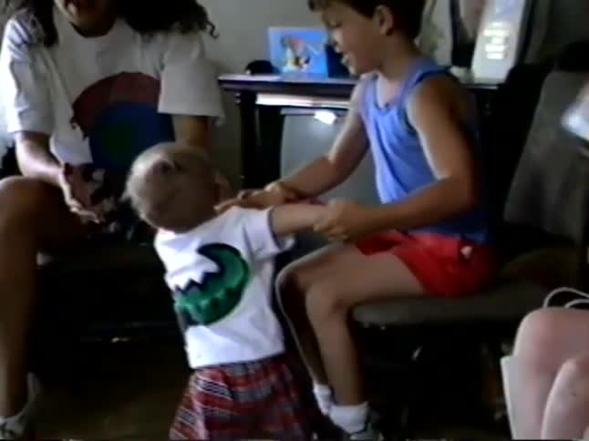 Nostalgic home video captures a heartwarming moment as a young boy plays with a toddler in a living room