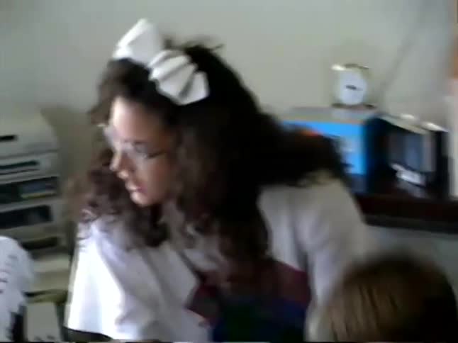 A young boy blows a party horn while sitting with his family in the living room during a 1990s home video