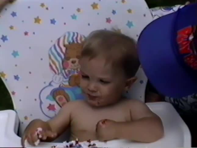 Adorable toddler in a high chair makes a happy mess while enjoying his first birthday cake
