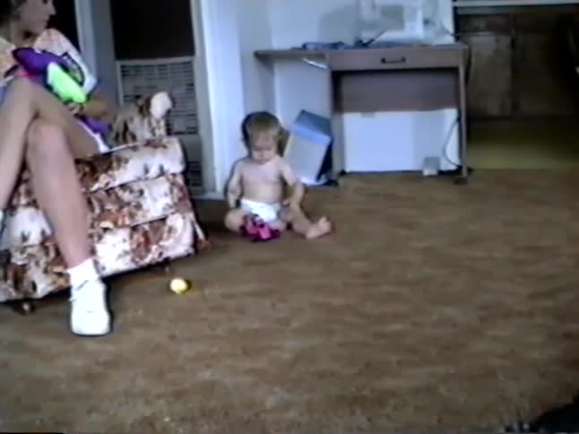 Vintage home video captures a curious baby in a diaper crawling across a brown carpet to play with a toy car
